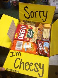 a person holding up a yellow box filled with snacks and candy that reads sorry, i'm cheesy