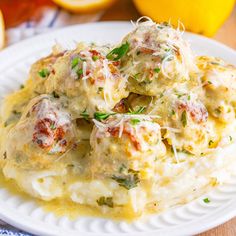 a white plate topped with mashed potatoes covered in meatballs and sauce next to sliced lemons