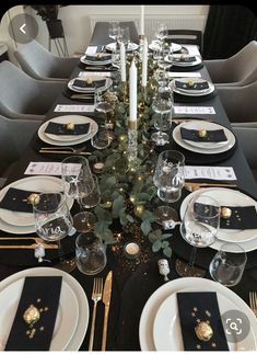 the table is set with black and white plates, silverware, candlesticks and greenery