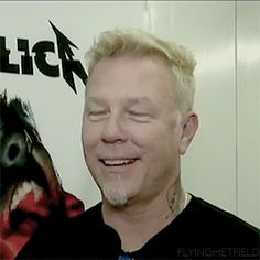 a man in black shirt standing next to a white wall with an image of a demon on it