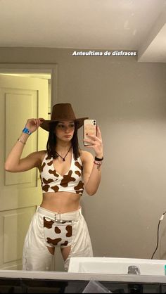 a woman taking a selfie in front of a mirror with her cell phone and cowboy hat