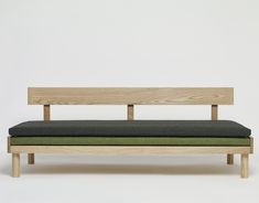 a wooden bench sitting on top of a white floor next to a green cushioned seat