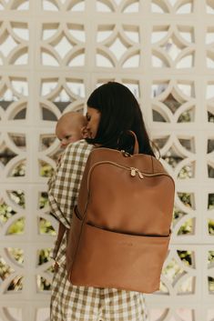 a woman holding a baby in her back pack while standing next to a white wall