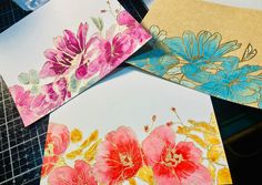 four cards with flowers painted on them sitting on a table next to some scissors and thread