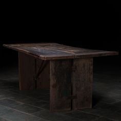 an old wooden table sitting on top of a tile floor next to a black wall