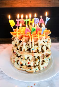 a birthday cake with lit candles on it sitting on top of a white platter