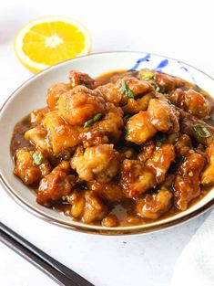 a white plate topped with chicken covered in gravy next to chopsticks