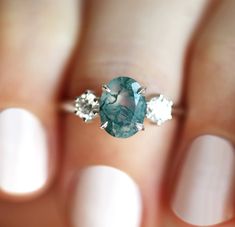 a woman's hand holding an aqua ring with three diamonds