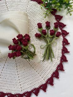 a crocheted doily with red flowers on it next to a white cloth