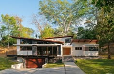 a modern house in the middle of a park with lots of trees and grass on both sides