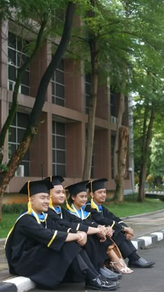 four men in graduation gowns are sitting on the curb