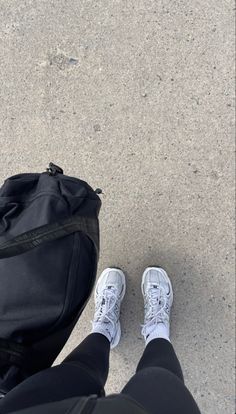 a person standing next to a black duffel bag on the ground with their feet propped up