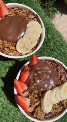 two bowls filled with granola, chocolate and strawberries on top of green grass