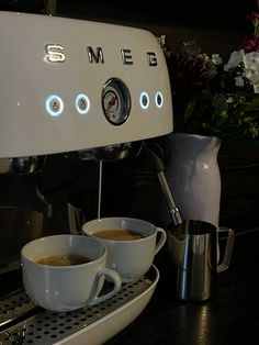 two cups of coffee sitting on top of a counter next to an espresso machine