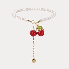 a white bracelet with two cherries on it and a gold charm hanging from the clasp