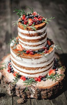 a three tiered cake with berries and greenery sits on top of a tree stump