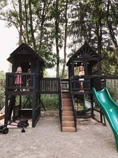 two girls are standing on the top of a play structure with a slide in front of them