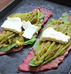 two pieces of meat with green beans and cheese on top, sitting on a baking sheet