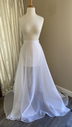 a white wedding dress on a mannequin in front of a window with sheer curtains