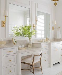 a white bathroom with gold accents and marble counter tops, along with two chairs in front of the vanity