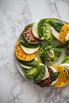 a white plate topped with sliced up tomatoes and cheese on top of a marble counter