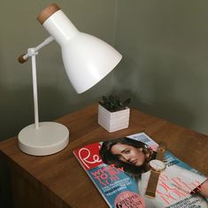 a magazine sitting on top of a wooden table next to a white lamp and potted plant