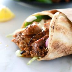 a burrito filled with meat and vegetables on top of a white plate next to a lemon wedge