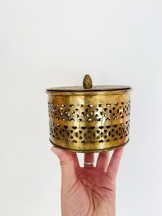 a hand holding a gold colored container with holes on it's sides and a golden lid