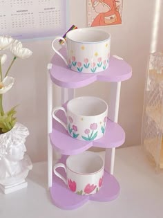 three tiered cup and saucer stand with flowers painted on the cups, next to a flower vase