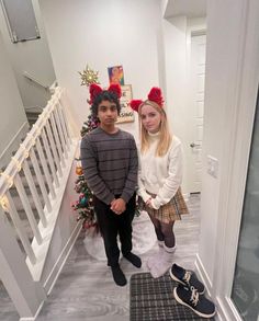 two people standing on the stairs in front of a christmas tree