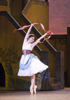 a ballerina is performing on stage with her arms in the air as she holds onto a ribbon