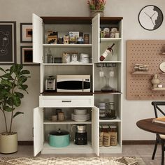 a kitchen with white cupboards filled with dishes and appliances next to a potted plant