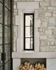 a fireplace with logs stacked in front of it and a window above the fire place