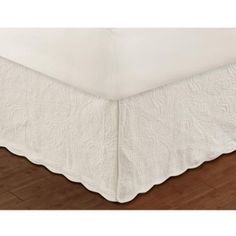 a white bed skirt on top of a wooden floor