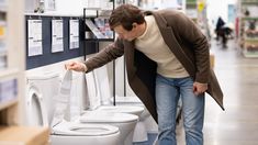 a man leaning over to pick up a toilet in a store with two toilets behind him