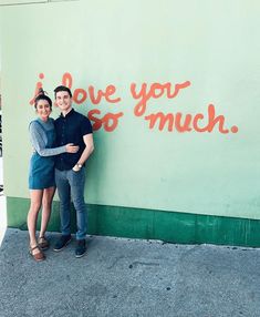 two people standing in front of a wall that says i love you so much