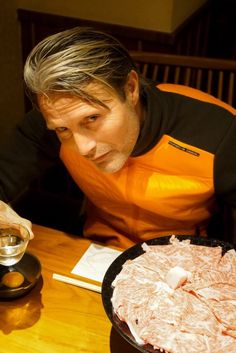 a man sitting at a table in front of a plate of meat and sauces