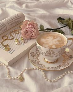 a cup of coffee on a saucer next to an open book and necklaces