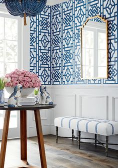 a room with blue and white wallpaper, a table with flowers on it and a mirror in the corner