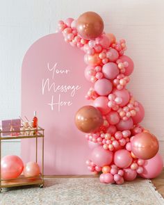 a pink and gold balloon arch with some balloons on the ground in front of it