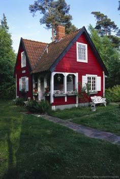 a red house with white trim and windows on the front porch is surrounded by trees