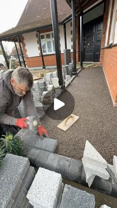 a man is working on some concrete blocks in front of a house with his hands