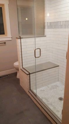 a walk in shower sitting next to a white toilet and tiled walls with glass doors