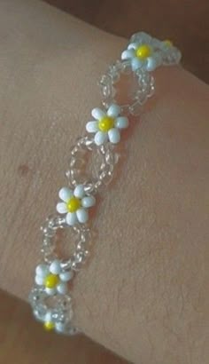 a woman's arm wearing a bracelet with white and yellow flowers on the side