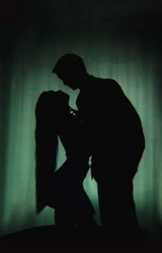 the silhouette of a man and woman kissing in front of a green curtained background