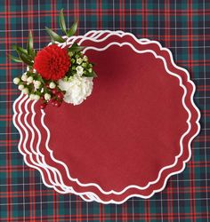 a red and white flower on top of a plaid table cloth with scalloped edges