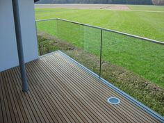 a wooden deck with glass railing and grass field in the background