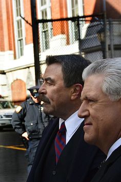 two men in suits and ties standing next to each other on the street with police officers behind them