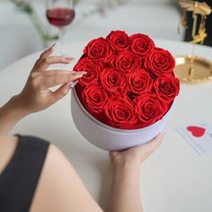 a woman holding a heart shaped box with red roses in it on top of a table