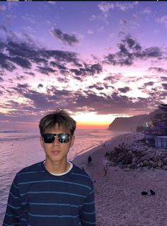 a man standing on top of a sandy beach next to the ocean at sunset with clouds in the sky